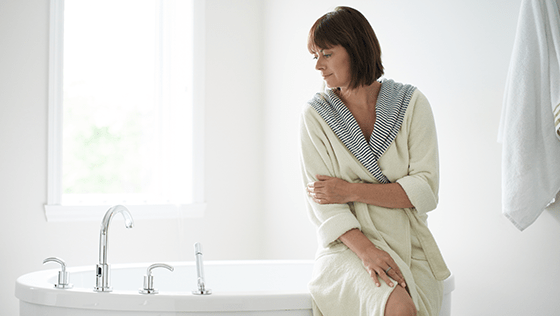 Woman holding her arm while sitting on the edge of a tub